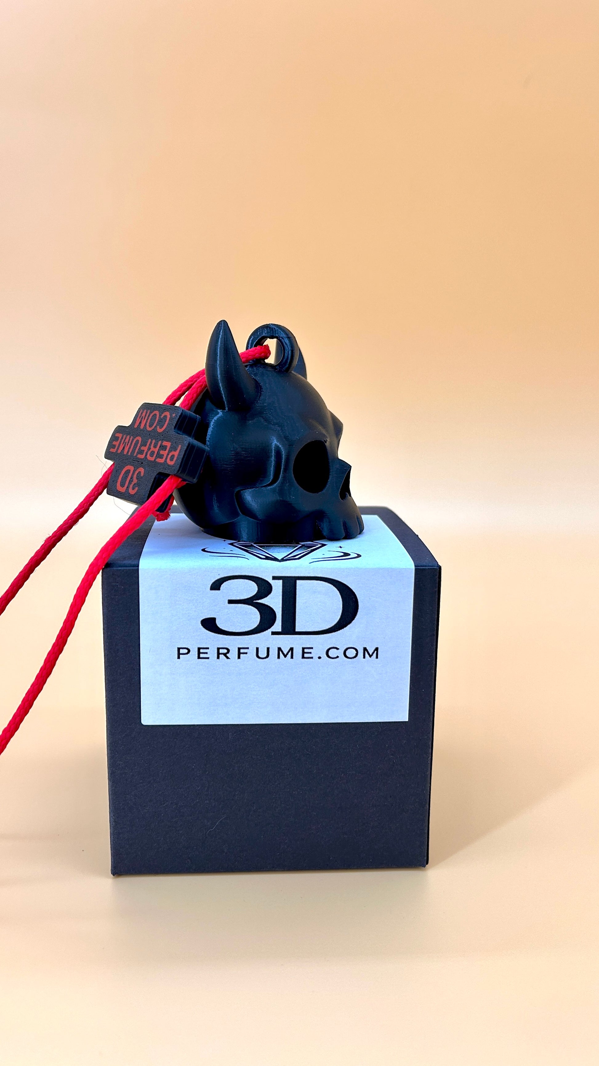Black skull-shaped perfume bottle with red accents on a 3D Perfume.com box against a beige background