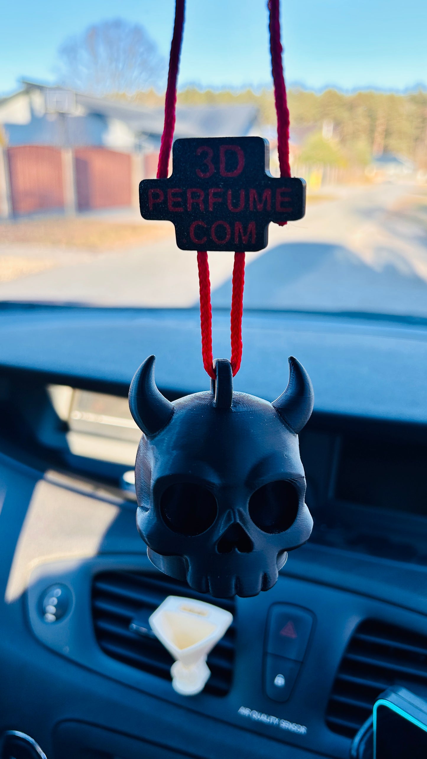 Skull-shaped car air freshener hanging from a red string on a car dashboard.
