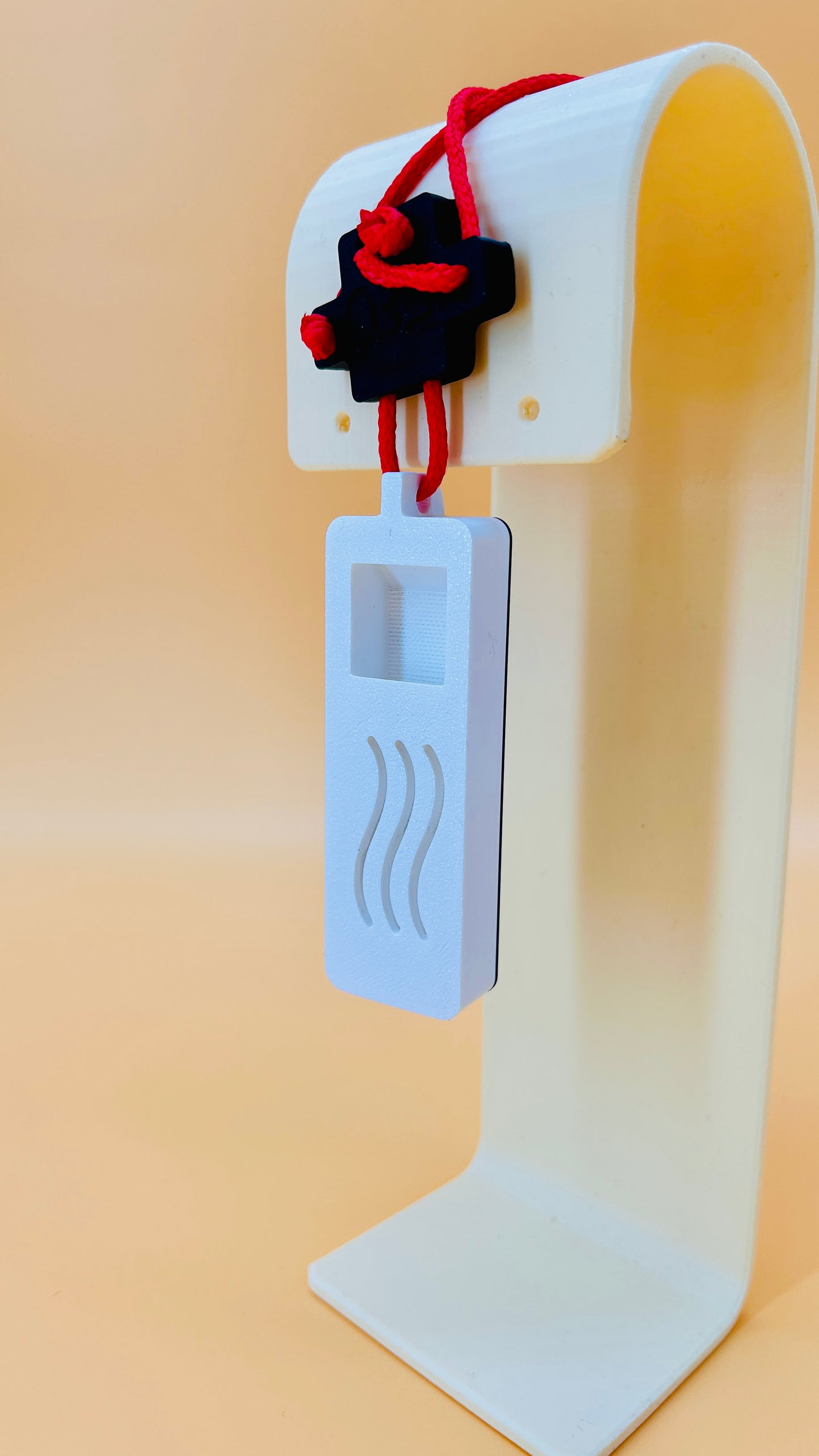 White 3D printed car air freshener with a red string and black object on a beige background