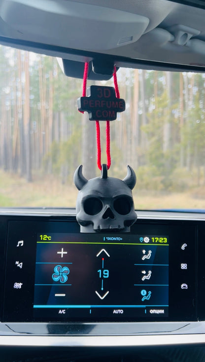 Car dashboard with a skull-shaped air freshener hanging from the rearview mirror, surrounded by trees outside.