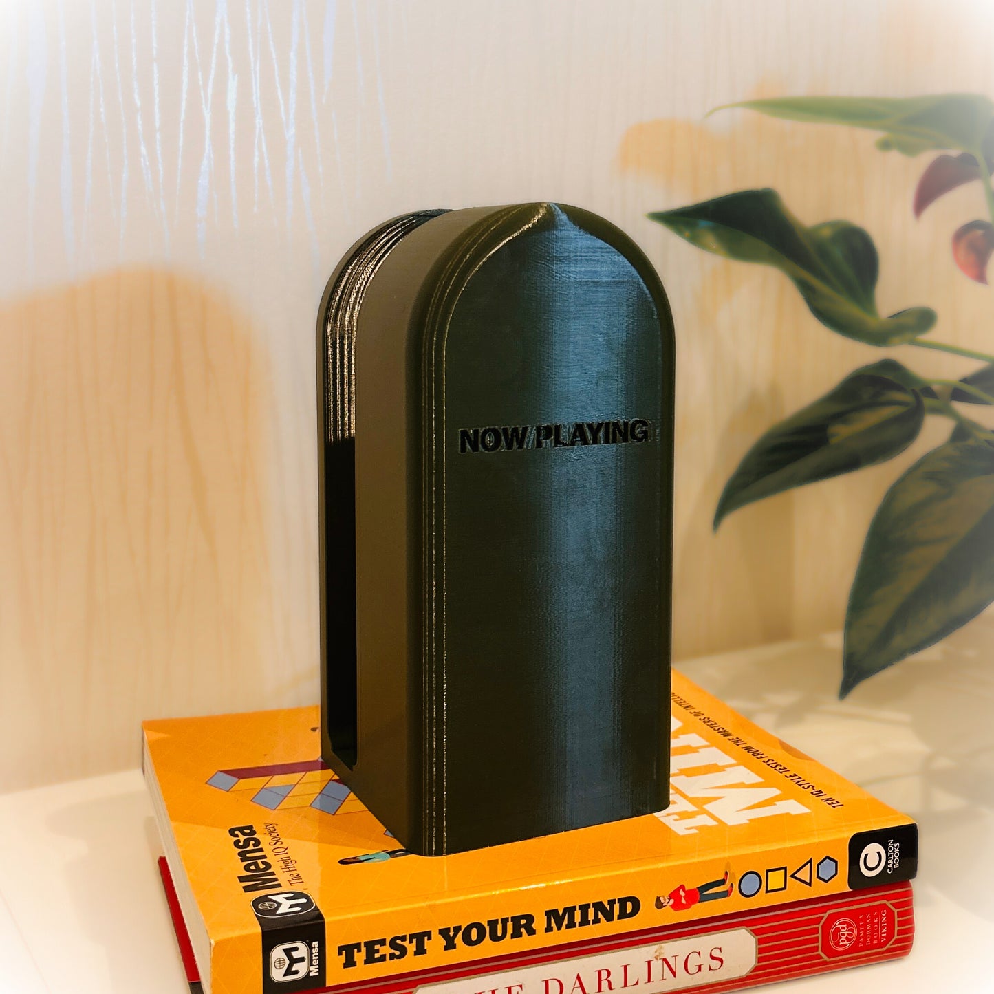 Black bookend with 'NOW PLAYING' on top of a book titled 'TEST YOUR MIND' on a surface.
