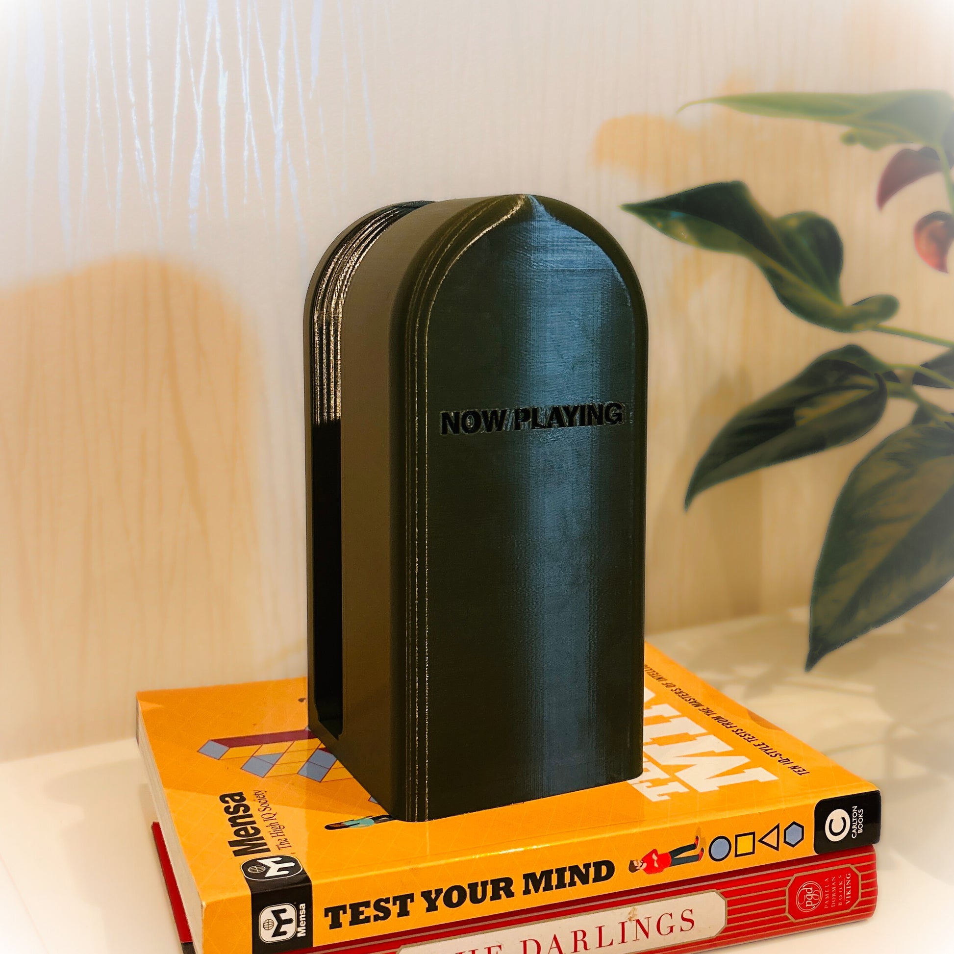 Black bookend with 'NOW PLAYING' on top of a book titled 'TEST YOUR MIND' on a surface.