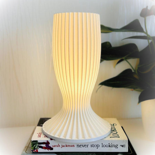 White textured table lamp on a book with a plant in the background